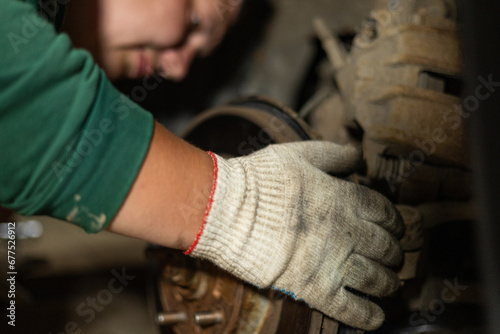 A man in work gloves repairs a wheel on a car in a garage. A man replaces a broken part on his car in the garage in the evening. Self-repair machine concept.