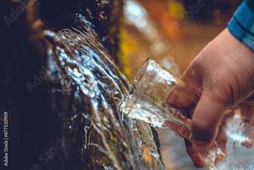 Bild auf Leinwand A hand brings a transparent bottle to a spring of drinking water