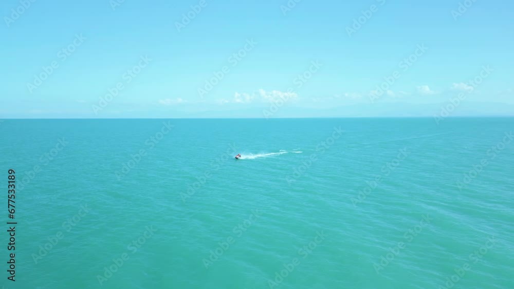 Aerial view of a man in a life jacket riding a jet ski on clear blue azure water on the sea. Sport, healthy lifestyle, outdoor recreation, vacation at sea, travel. Lake Sevan, Armenia. Aerial view of a man in a life jacket riding a jet ski on clear blue azure water on the sea. Sport, healthy lifestyle, outdoor recreation, vacation at sea, travel. Lake Sevan, Armenia.