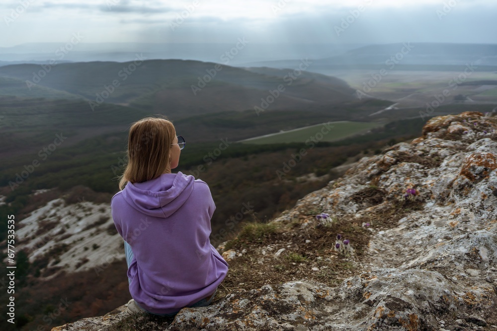 Naklejka premium Girl on mountain peak looking at beautiful mountain valley in fog at sunset in summer. Landscape with sporty young woman, foggy hills, forest, sky. Travel and tourism, hiking