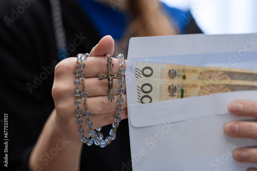 Modląca się kobieta trzyma w dłoni kopertę z pieniędzmi w dużych nominałach  photo