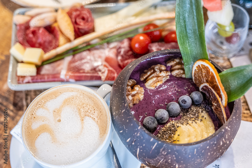 A delicious Açaí bowl adorned with luscious blueberries and crunchy nuts, presented within a unique coconut shell cup and a plate of ham and cheese an a cup of coffee for healthy breakfast or brunch. A delicious Açaí bowl adorned with luscious blueberries and crunchy nuts, presented within a unique coconut shell cup and a plate of ham and cheese an a cup of coffee for healthy breakfast or brunch.