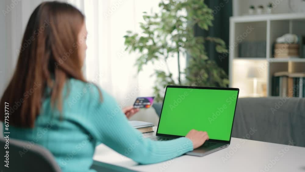 Woman's hand holds credit card while typing on laptop keyboard with green screen, concept e-commerce, chroma, payment, internet banking