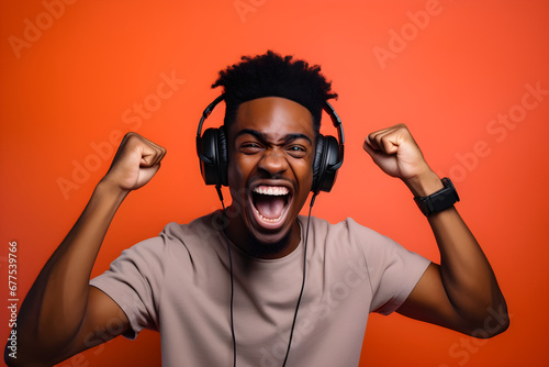 studio portrait of happy gamer black man wearing headphones celebrating on orange background
 photo