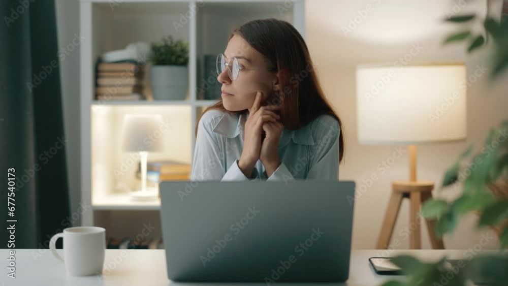 Woman seated at home on remote work, typing on laptop, occasionally gazes out of window, lost in thought Woman seated at home on remote work, typing on laptop, occasionally gazes out of window, lost in thought