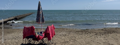Molo su una spiaggia con ombrellone chiuso ed asciugamano su una sedia e sfondo del mare