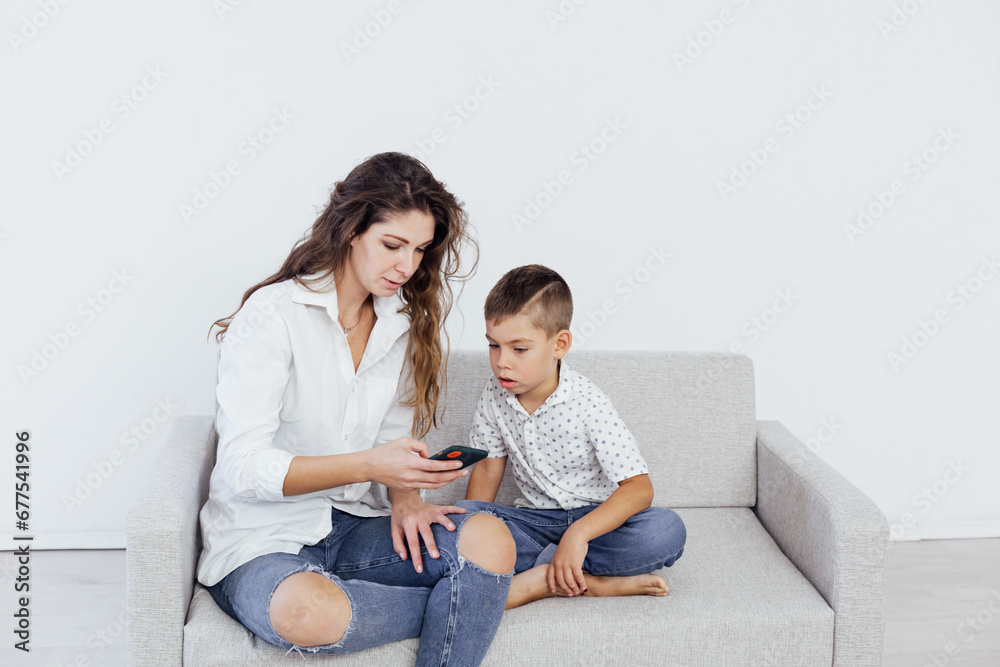 mother and son sit on the couch with a phone in a bright room