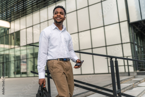 With purpose in his stride, the stylish African-American businessman carries his laptop bag and holds his phone, ready to conquer the day's challenges.