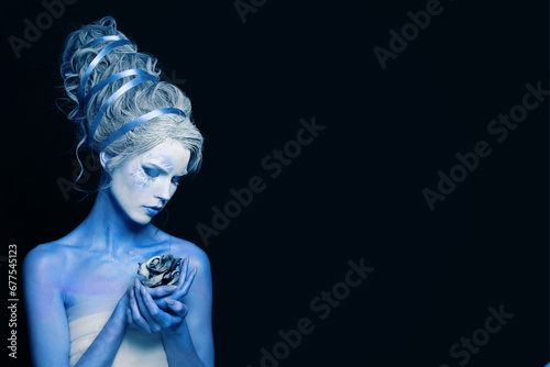 Attractive cool woman with blue and white body art, carnival makeup and hairstyle holding rose flower on black background photo