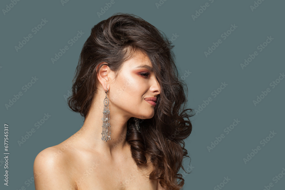 Naklejka premium Lovely jewelry model. Beautiful woman with wavy hair and luxurious earring posing on blue background