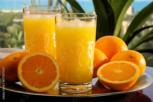 a glass of orange juice and oranges, whole and sliced, on the balcony on a bright day, a delicious refreshing drink
