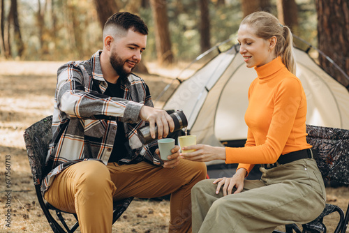 Couple drinking tea by their tent in forest