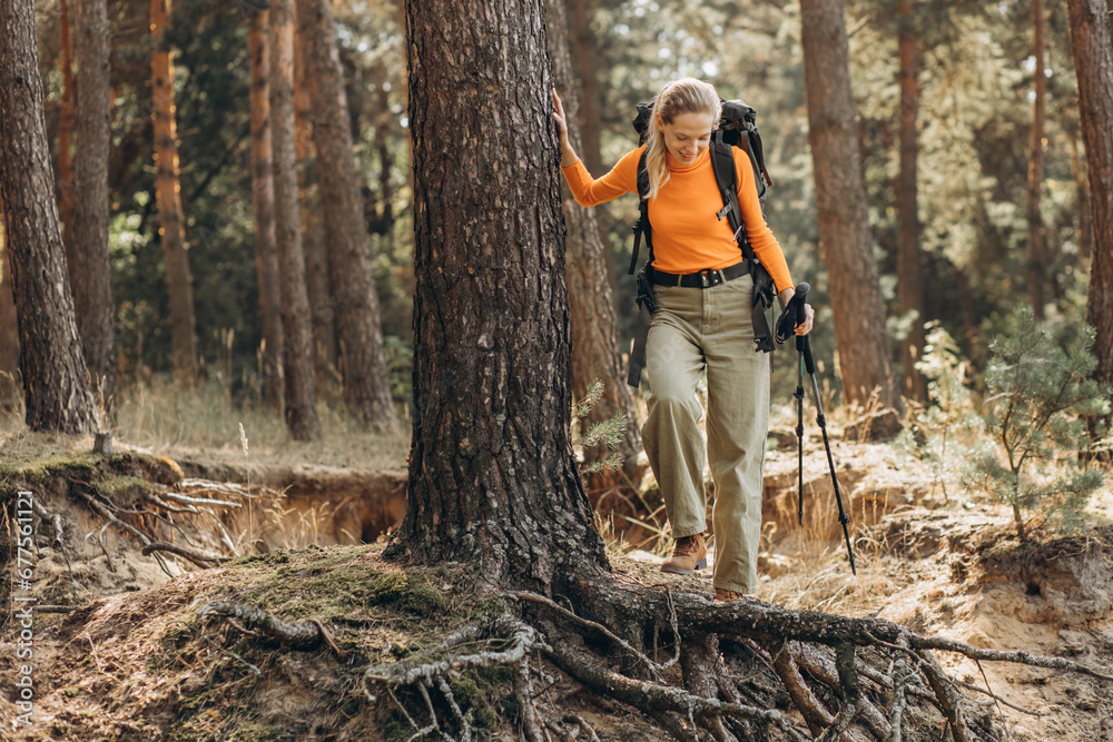 Woman hiking with walking sticks in forest stopped by the tree Woman hiking with walking sticks in forest stopped by the tree