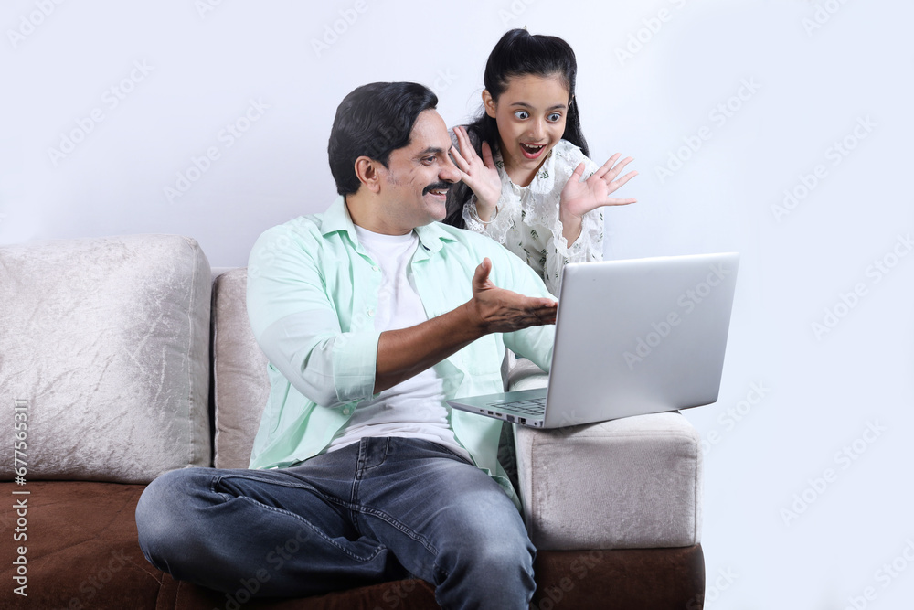 Happy Indian family of single father and daughter surfing laptop having pleasant time together joyfully. Family is looking into the laptop, both surprised. Happy Indian family of single father and daughter surfing laptop having pleasant time together joyfully. Family is looking into the laptop, both surprised.