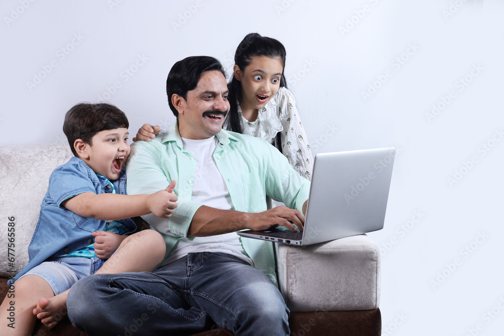 Happy Indian family of father, son and daughter surfing laptop having pleasant time together joyfully. Family is looking into the laptop, surprised, shocked. Happy Indian family of father, son and daughter surfing laptop having pleasant time together joyfully. Family is looking into the laptop, surprised, shocked.