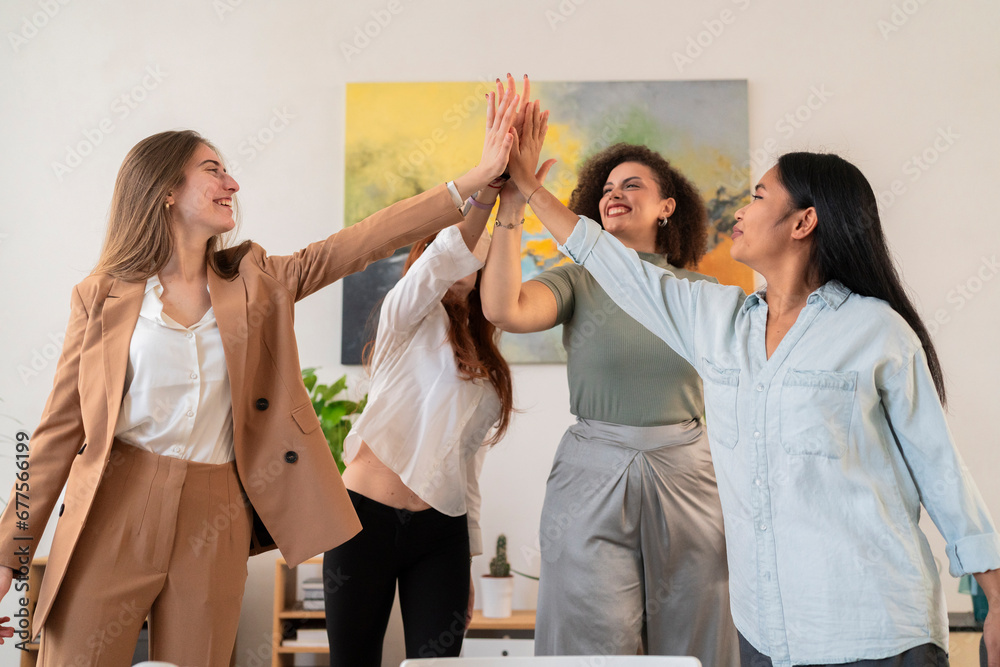 © Studio Marmellata - Happy young women colleagues standing and giving high five to each other while celebrating success in modern creative office during business meeting