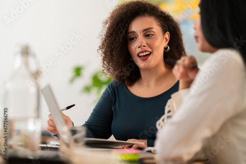 Concentrated young females colleagues in casual clothes sitting at wooden table with laptop working on project while discussing details of new business photo