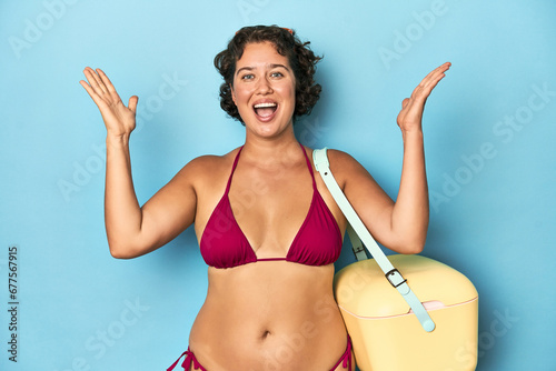 Young woman with cooler and summer look receiving a pleasant surprise, excited and raising hands. photo