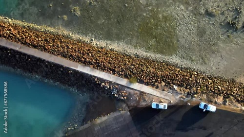A longer overhead drone shot, showing the rocky seawall leading through the lowtide mudflats into the vivid blue water.  Filmed in 4K. photo
