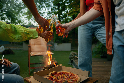 Friends toasting having picnic drinking beer and eating pizza nearby bonfire