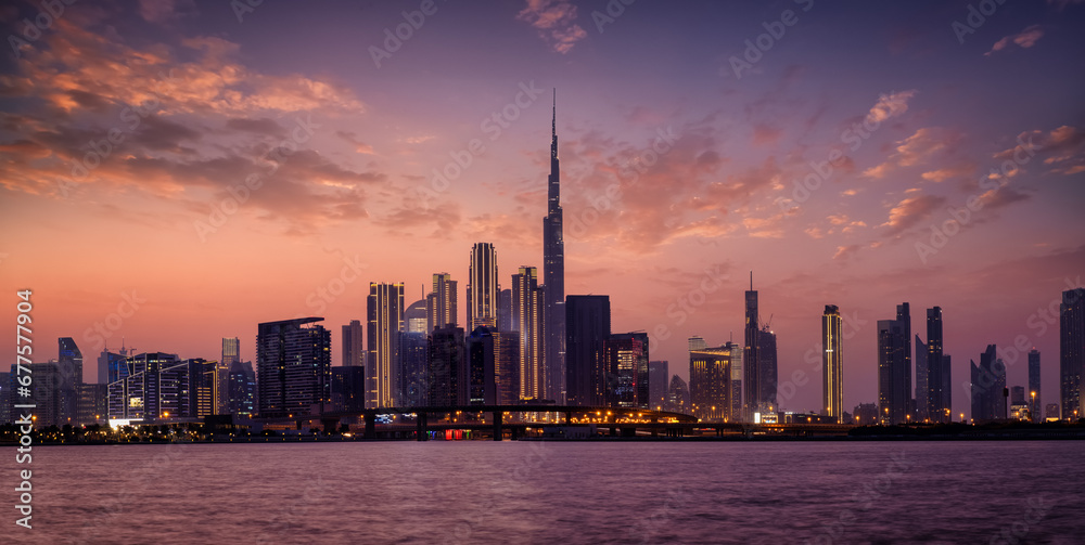 Panoramic view of the illuminated skyline of Dubai Business bay with reflections of the modern skyscrapers in the water during dusk time, UAE