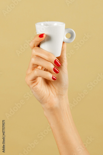 Unrecognizable woman holding coffee cup in hand against brown backdrop