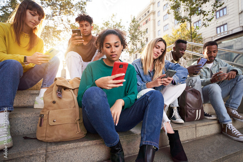 Diverse group of university friends sitting on street staircase, serious students people using and looking at smart phones. Photo shows addiction to new technologies and social networks, generation Z. photo