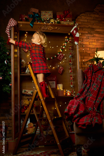 Merry Christmas and Happy Holiday. A little girl in a plaid dress climbs the stairs to the top shelf of a closet with gifts. Atmosphere of magic, enchantment and celebration
