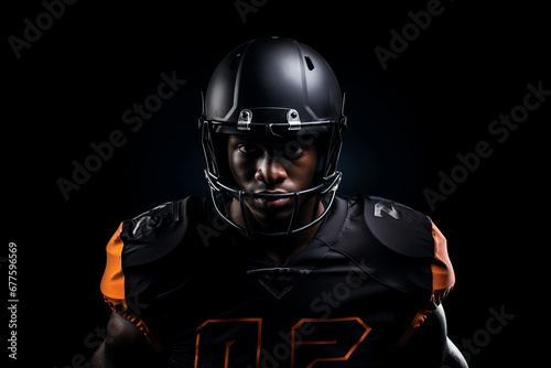 Studio portrait of professional American football player in black uniform. Determined, powerful, skilled African American athlete wearing helmet with protective mask. Isolated in black background. © Georgii