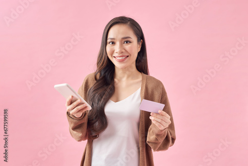 Pleased young woman posing isolated over pink wall background using mobile phone holding debit card.
