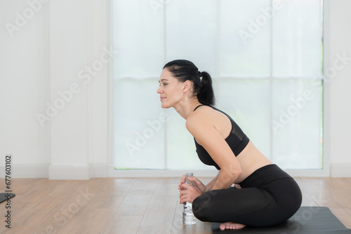 Young women sitting rest on yoga mats and drinking water. They are looking at each other and smiling