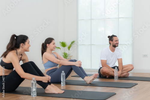 A group of female and male athletes sitting rest on yoga mats and drinking water. They are looking at each other and smiling