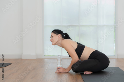 Young women sitting rest on yoga mats and drinking water. They are looking at each other and smiling