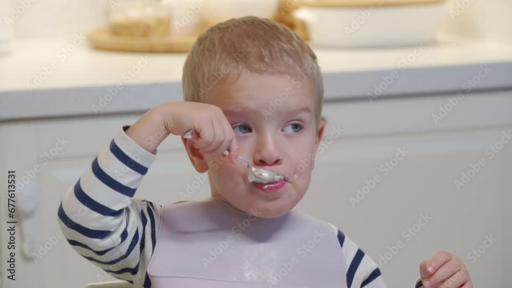 toddler child little boy eating yogurt sitting at the dining table and watching TV at home toddler child little boy eating yogurt sitting at the dining table and watching TV at home