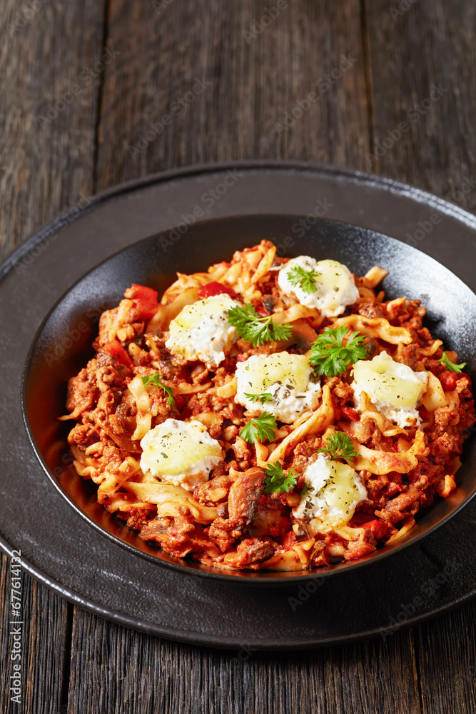 Lasagnette with beef ragu, mushrooms and ricotta cheese in black bowl on dark wooden table, italian recipe, vertical view from above, close-up Lasagnette with beef ragu, mushrooms and ricotta cheese in black bowl on dark wooden table, italian recipe, vertical view from above, close-up