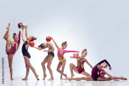 Group of beautiful little girls, children, rhythmic gymnasts in stage clothes dancing with balls against white studio background. Concept of choreography, hobby, art, sport, childhood, performance photo