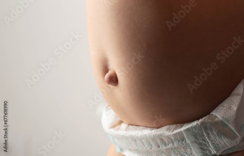 Baby belly with bulging navel on a gray background. Umbilical hernia in newborns, dilated umbilical ring, medical. Copy space for text