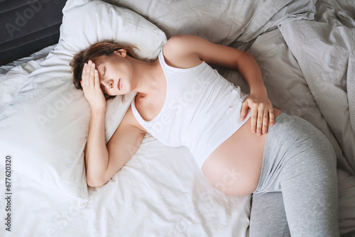 Exhausted pregnant woman suffering from insomnia or pain lying in bed. photo