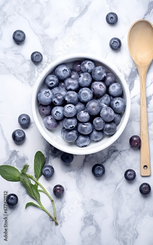 A bowl of blueberries on a marble surface next to a wooden spoon and green leaves.
