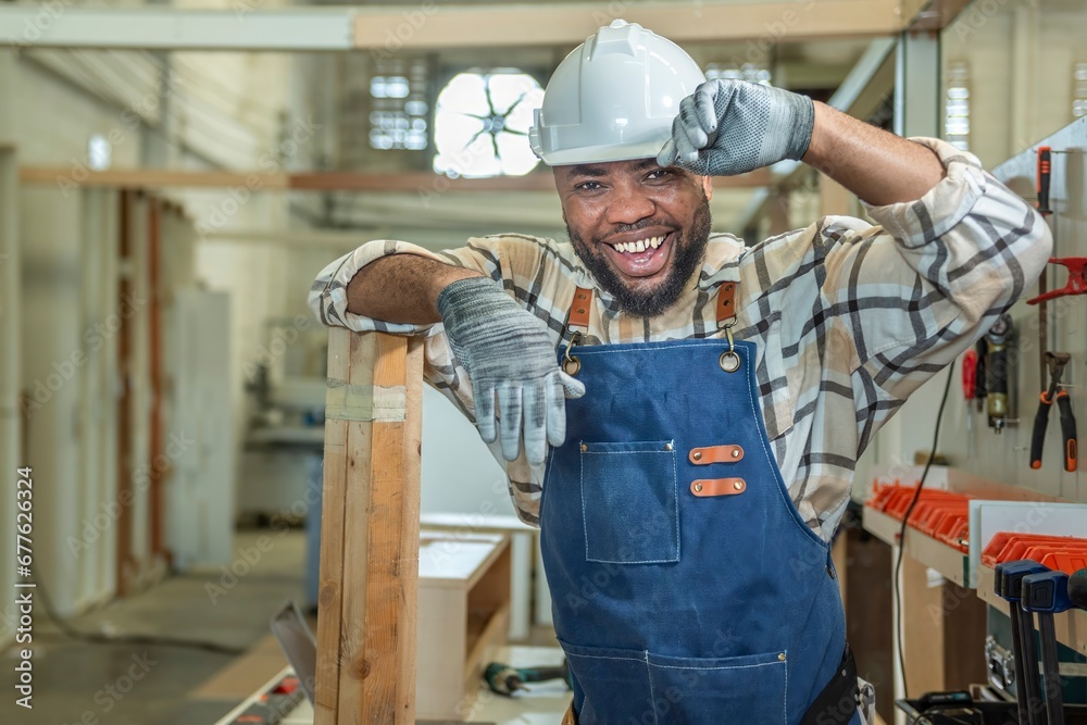 Carpenter man Portrait of Young black skin looking smile laugh to camera in workshop. Happy professional Carpenter holds wooden planks for build furniture in carpentry workshop. one carpenter worker Carpenter man Portrait of Young black skin looking smile laugh to camera in workshop. Happy professional Carpenter holds wooden planks for build furniture in carpentry workshop. one carpenter worker