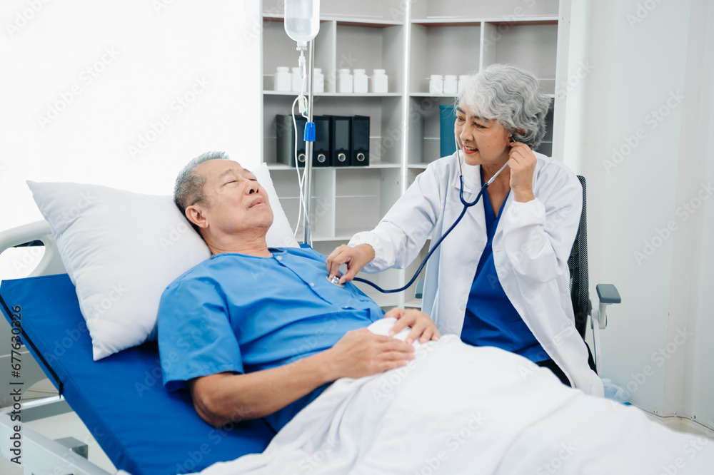 Asian doctor in white suit take notes while discussing and Asian elderly, man patient who lying on bed with receiving saline solution Asian doctor in white suit take notes while discussing and Asian elderly, man patient who lying on bed with receiving saline solution
