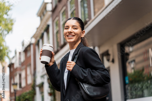 Stressless multiracial young businesswoman with a cheerful expression, in the street, holding a thermo cup of coffee photo