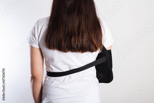 A girl on a white background with a black supporting medical bandage after a dislocation of the shoulder joint and a bone fracture. Rehabilitation after injury, orthopedics and traumatology photo