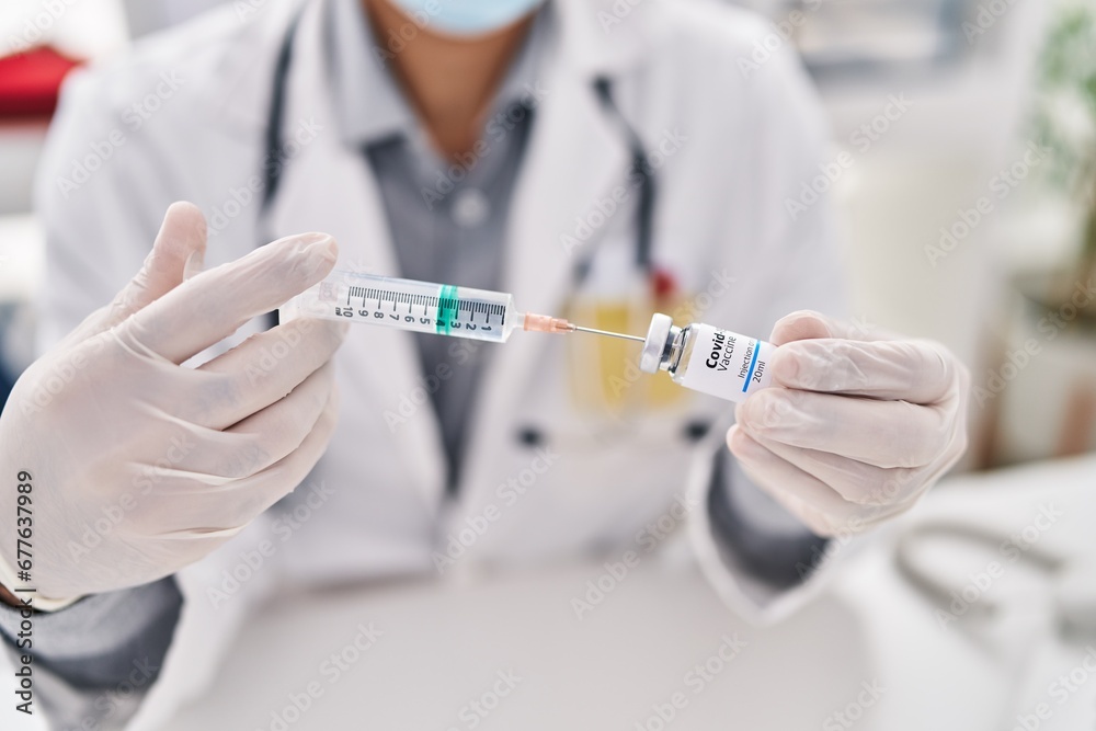 Young hispanic man doctor holding covid vaccine at clinic Young hispanic man doctor holding covid vaccine at clinic