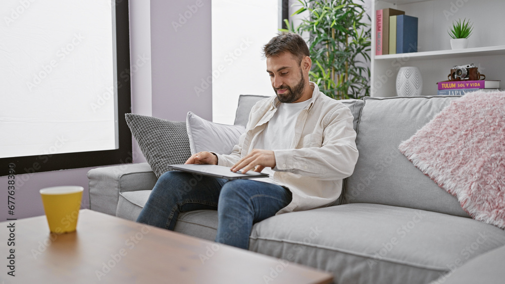 Young hispanic man closing laptop sitting on sofa at home