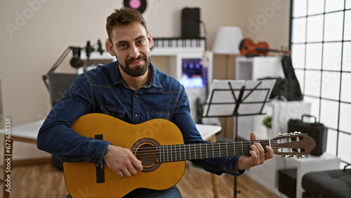 Soulful strumming by smiling young hispanic man, classic melody immersed in music studio performance on acoustic guitar photo