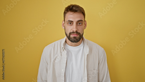 Fotografie Young hispanic man standing with serious expression over isolated yellow backgro