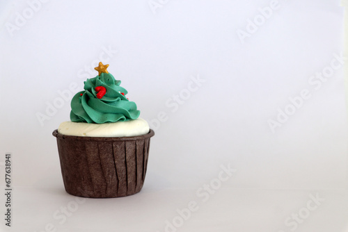 Cupcakes decorated with green buttercream. It is a Christmas tree pattern, which has a gold star atop, in a brown cup. Placed on a white background.