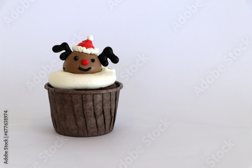 Cupcakes decorated with buttercream. It is a reindeer pattern and a Christmas hat on the head, in a brown cup. Placed on a white background.