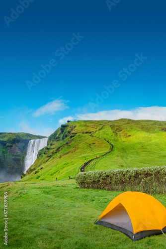 Cover page camping site with orange tent  and tourists in front of famous Skogafoss waterfall  while hiking in Iceland  summer  scenic view  with copy space